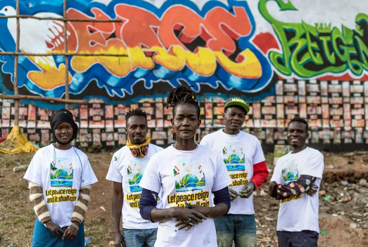 Campaigners in "Let peace reign" T-shirts in front of a peace mural